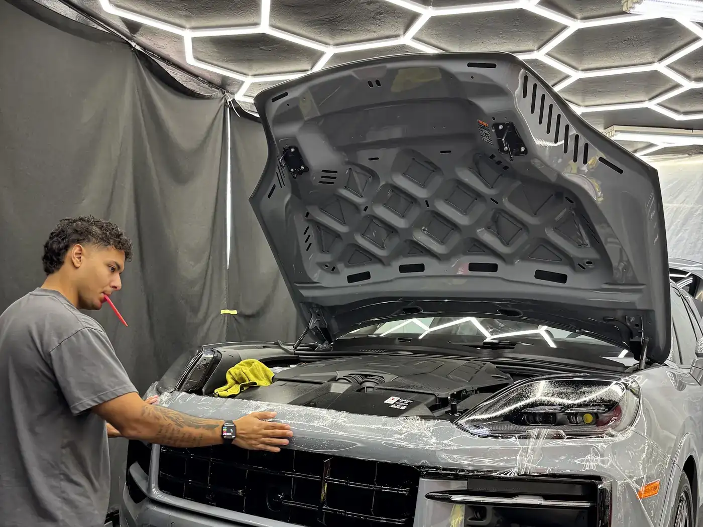 Technician squeegeeing film onto a Porsche bumper under the hexagon ceiling lights